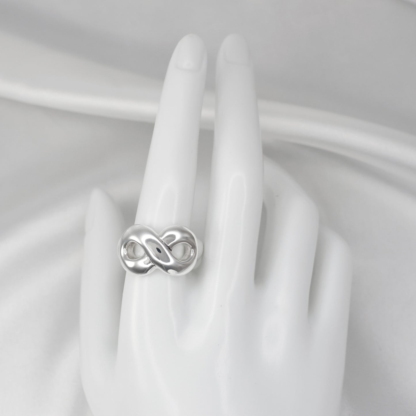 Chunky silver infinity statement ring displayed on a white hand model for elegant jewelry styling