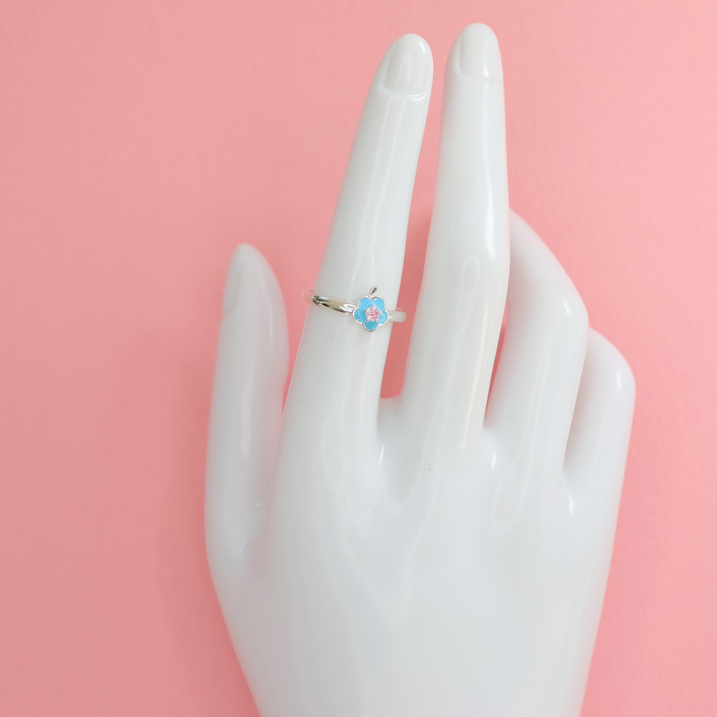 Floral design silver ring with delicate flower detail on a hand model against a pink background