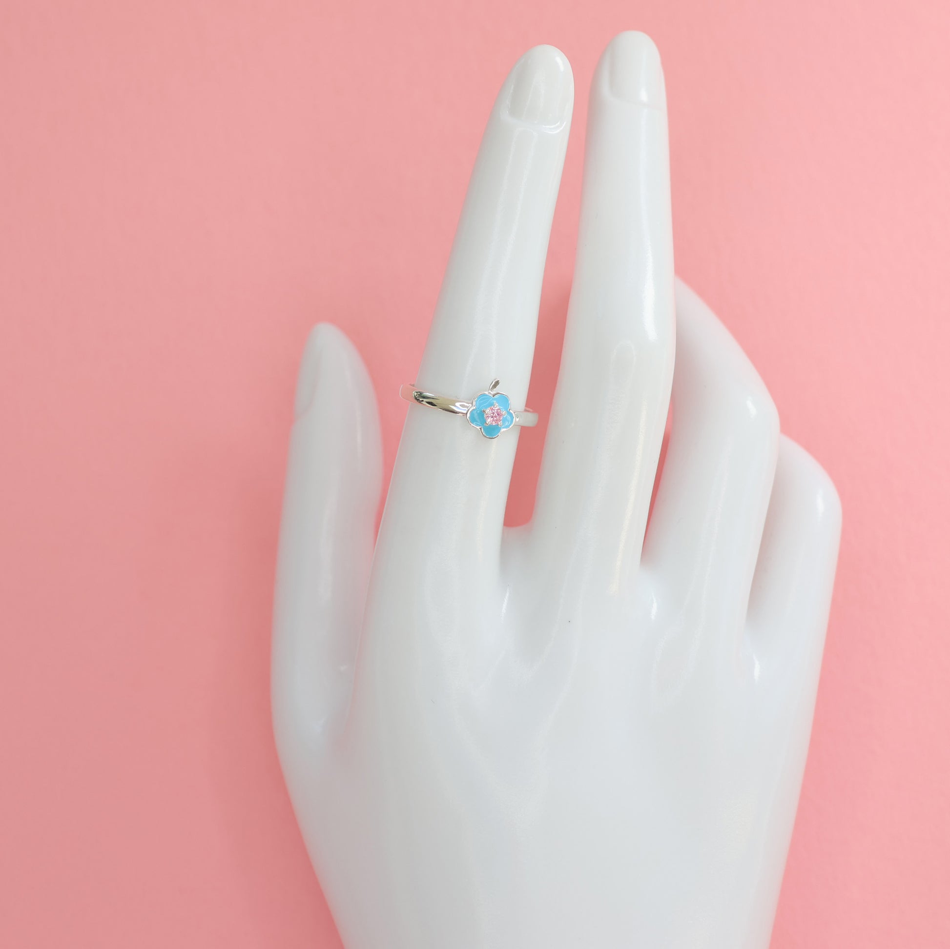 Floral design silver ring with delicate flower detail on a hand model against a pink background
