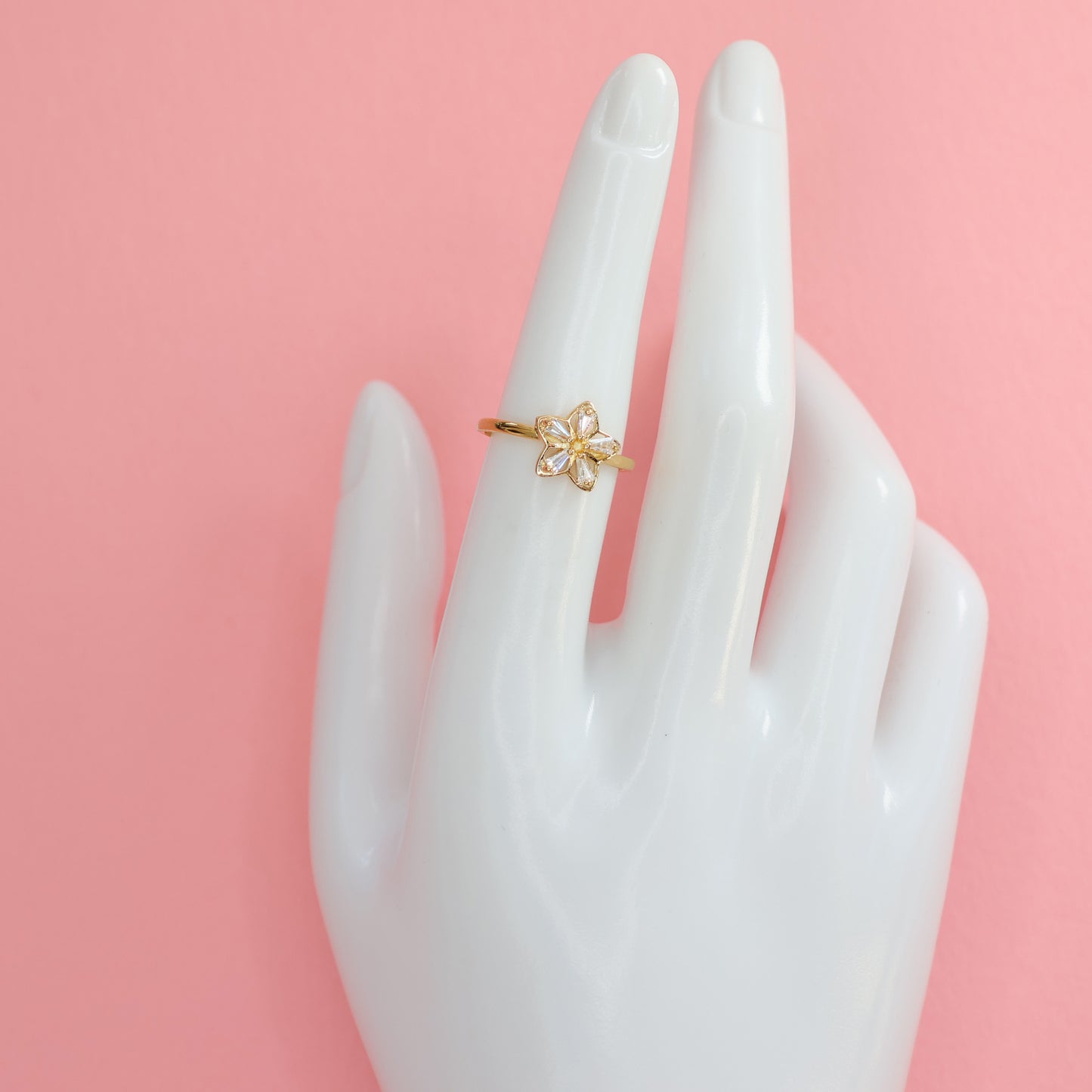 Elegant flower design gold plated ring showcased on a mannequin hand against a pink background