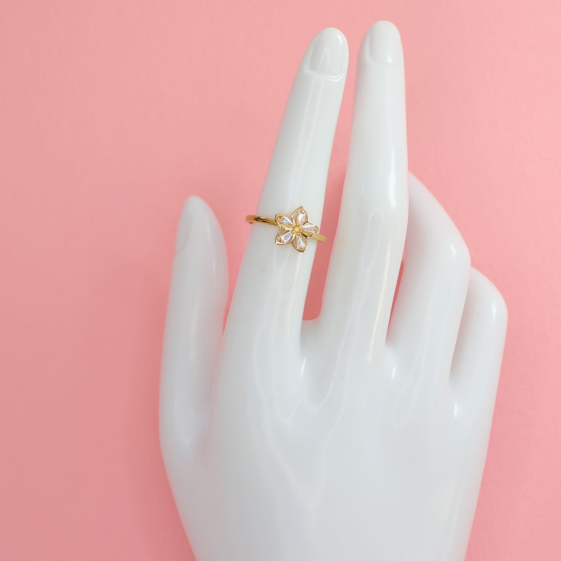 Elegant flower design gold plated ring showcased on a mannequin hand against a pink background
