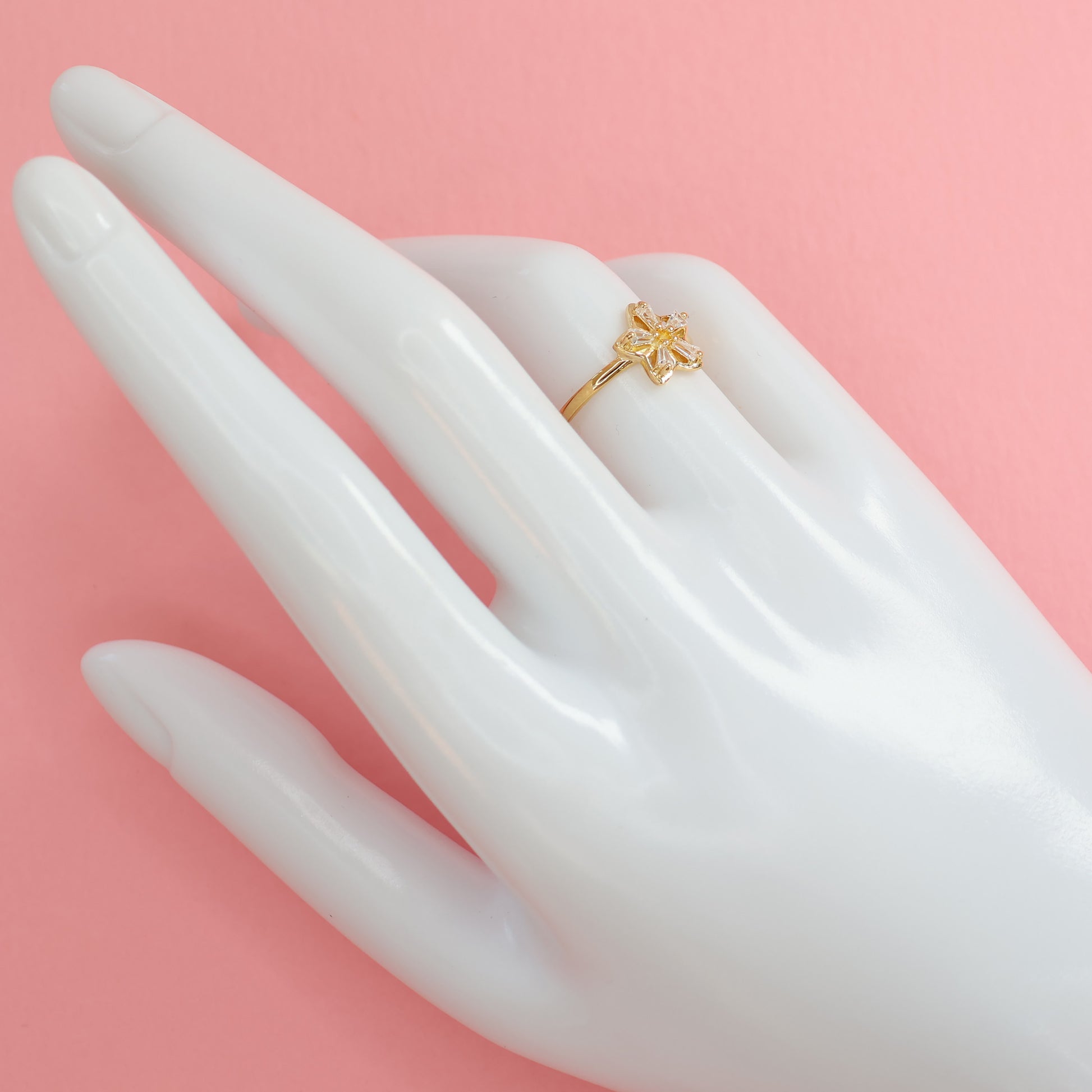 Elegant flower design gold plated ring displayed on a mannequin hand with a soft pink background