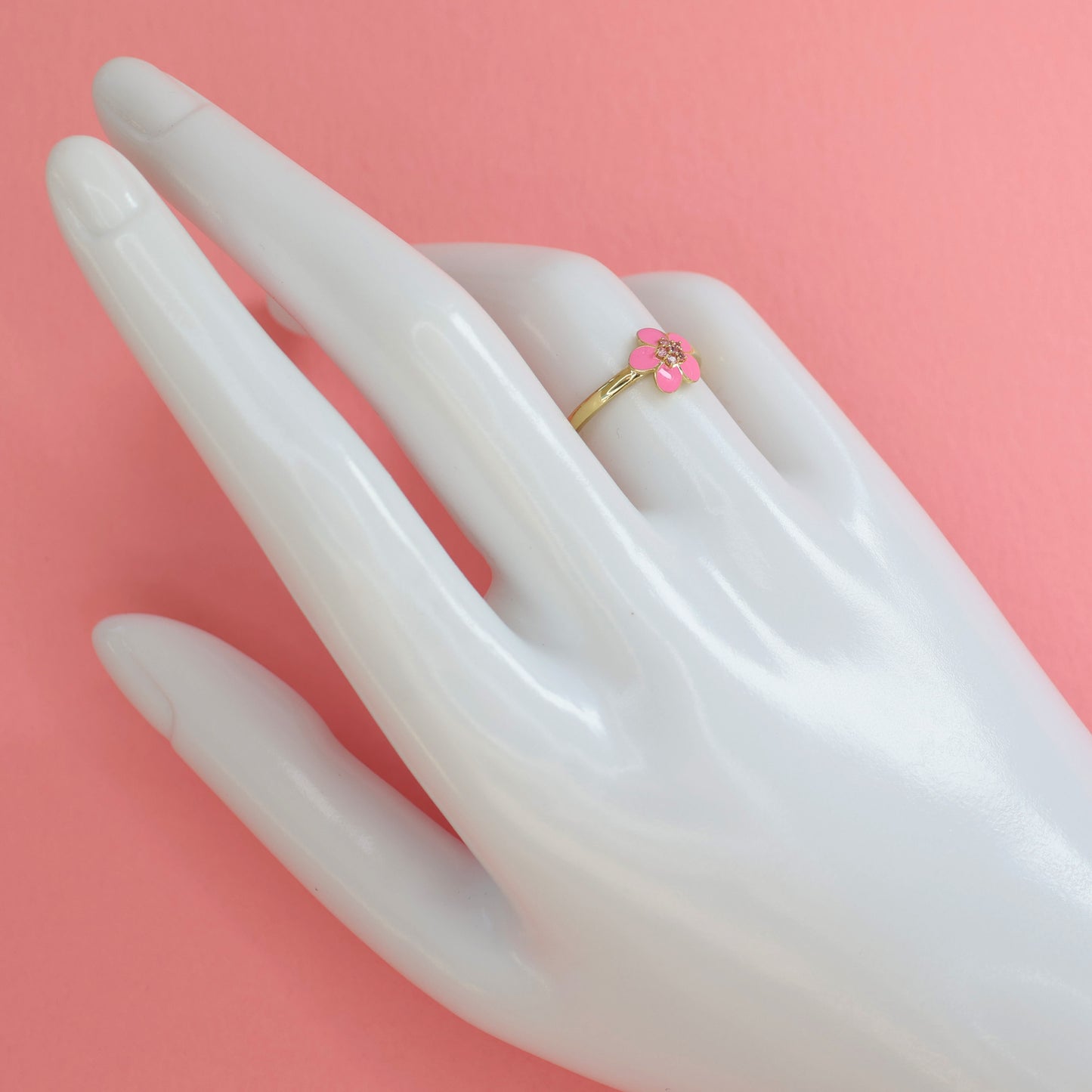 Gold plated pink enamel ring displayed on a white hand model against a pink background