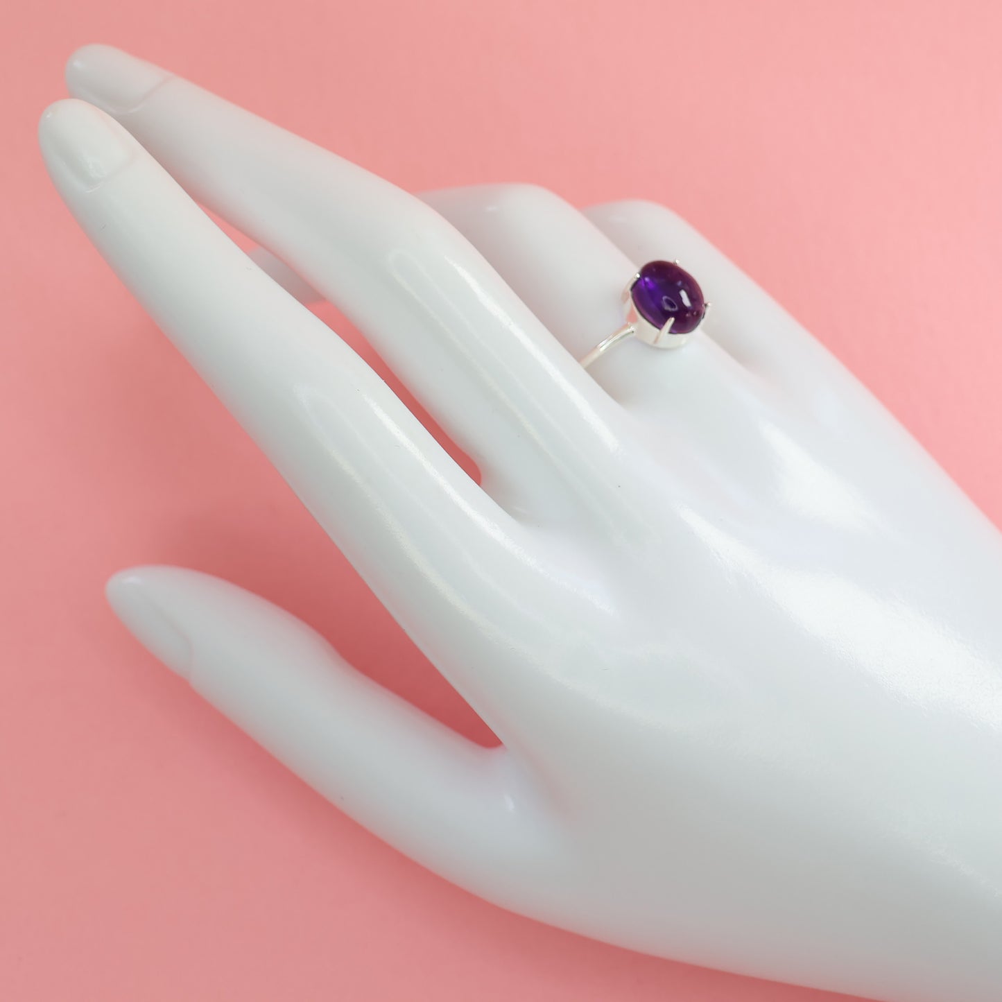 Elegant large amethyst silver ring displayed on a hand mannequin with a pink background