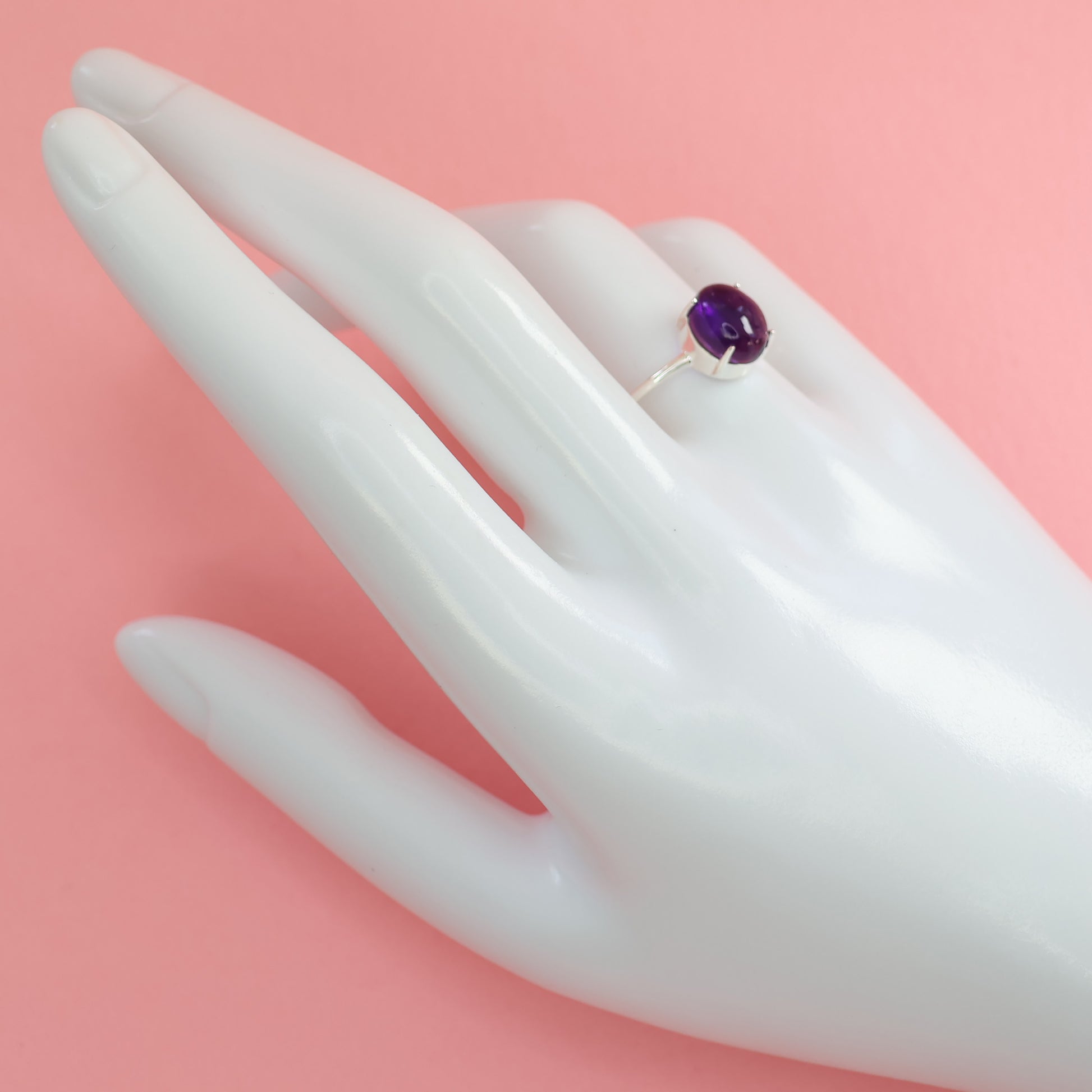 Elegant large amethyst silver ring displayed on a hand mannequin with a pink background