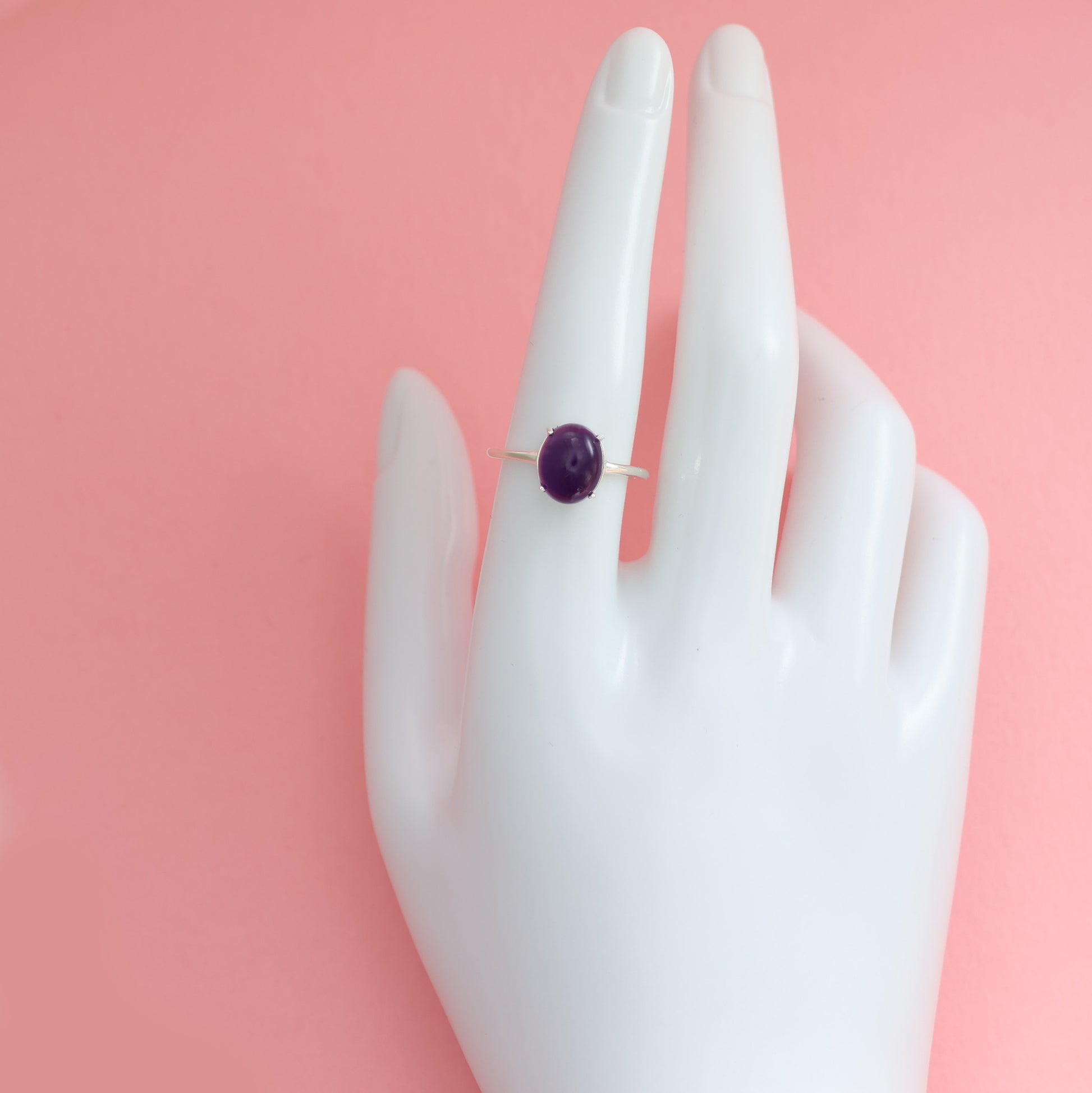 Large amethyst silver ring displayed on a hand model against a pink background