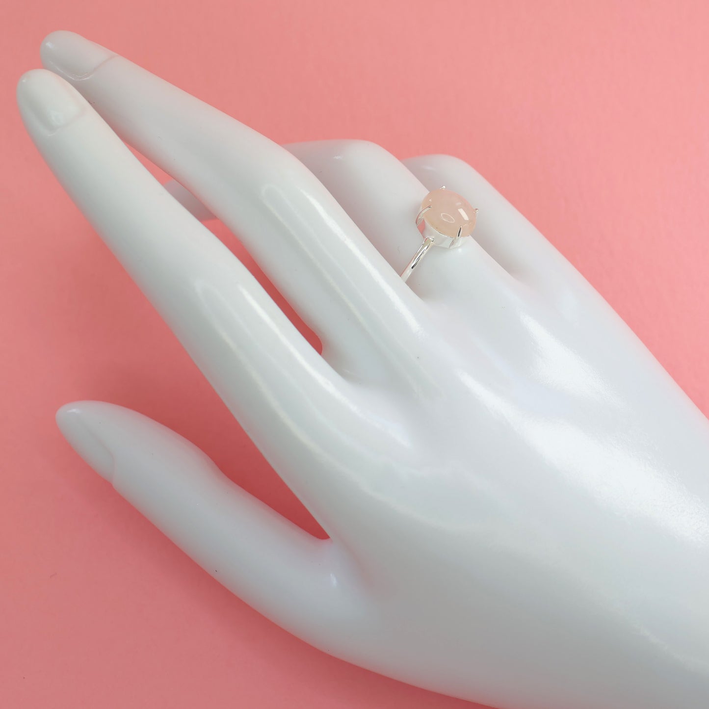 Elegant large rose quartz silver ring displayed on a hand against a pink background