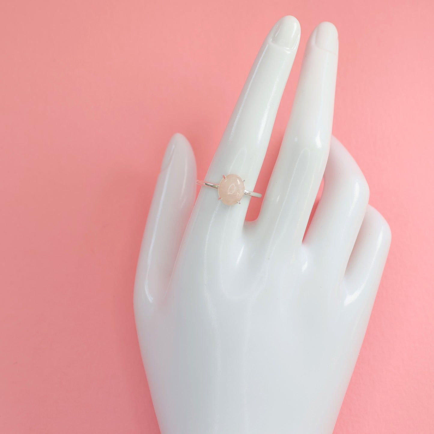 Large rose quartz silver ring displayed on a hand mannequin against a pink background