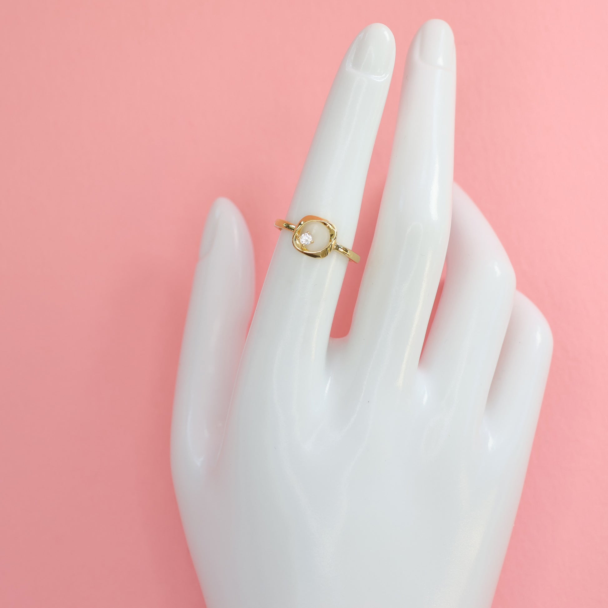 Elegant modern square ring with CZ stone displayed on a hand mannequin against a pink background