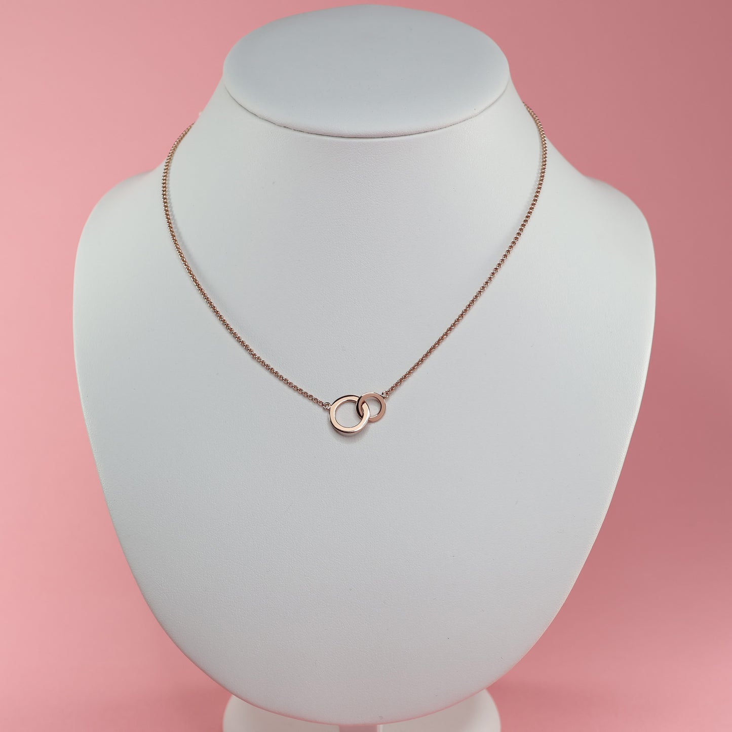 Elegant rose gold double hoop pendant necklace on a display bust against a pink background