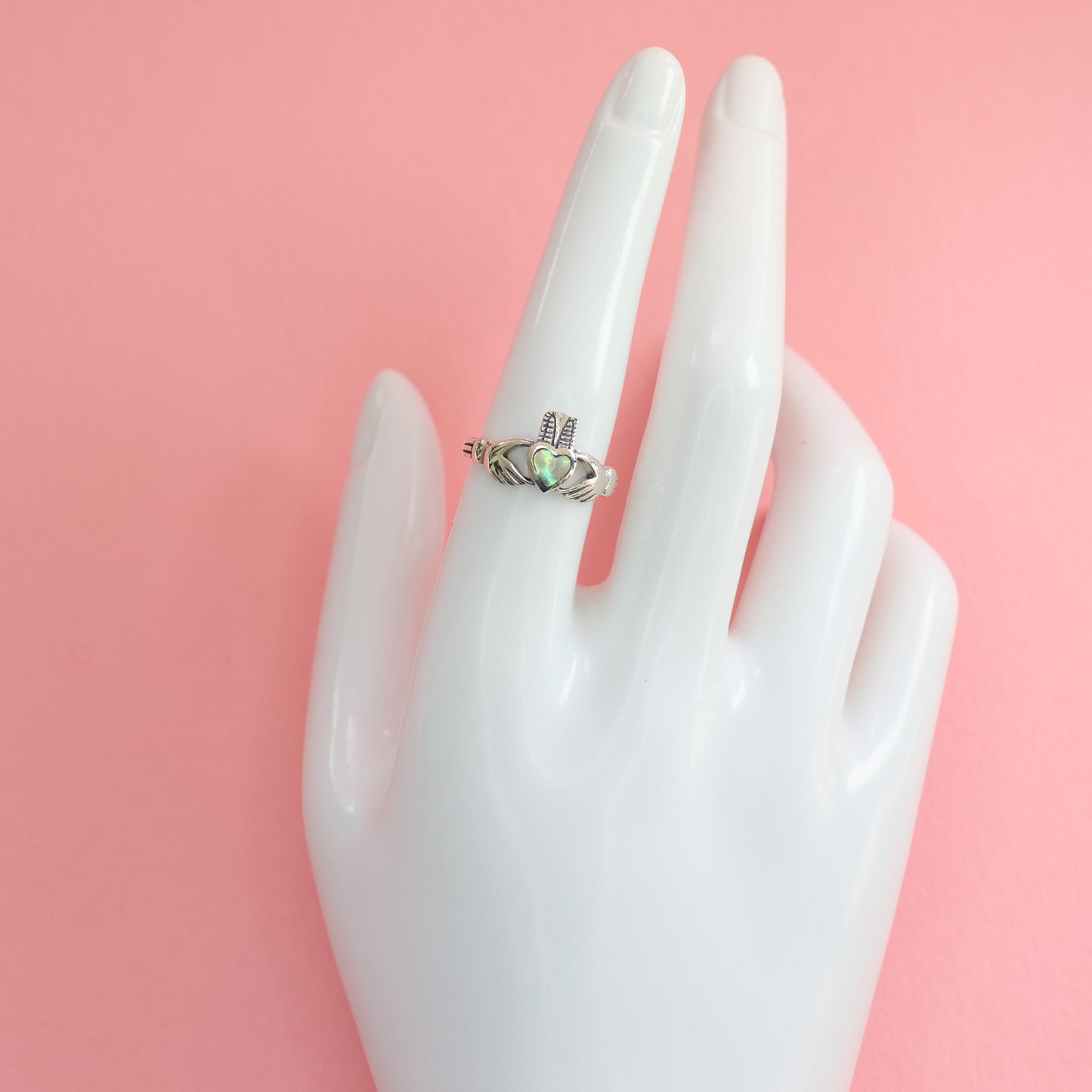 Stylish Silver Claddagh Ring displayed on a hand mannequin against a pink background