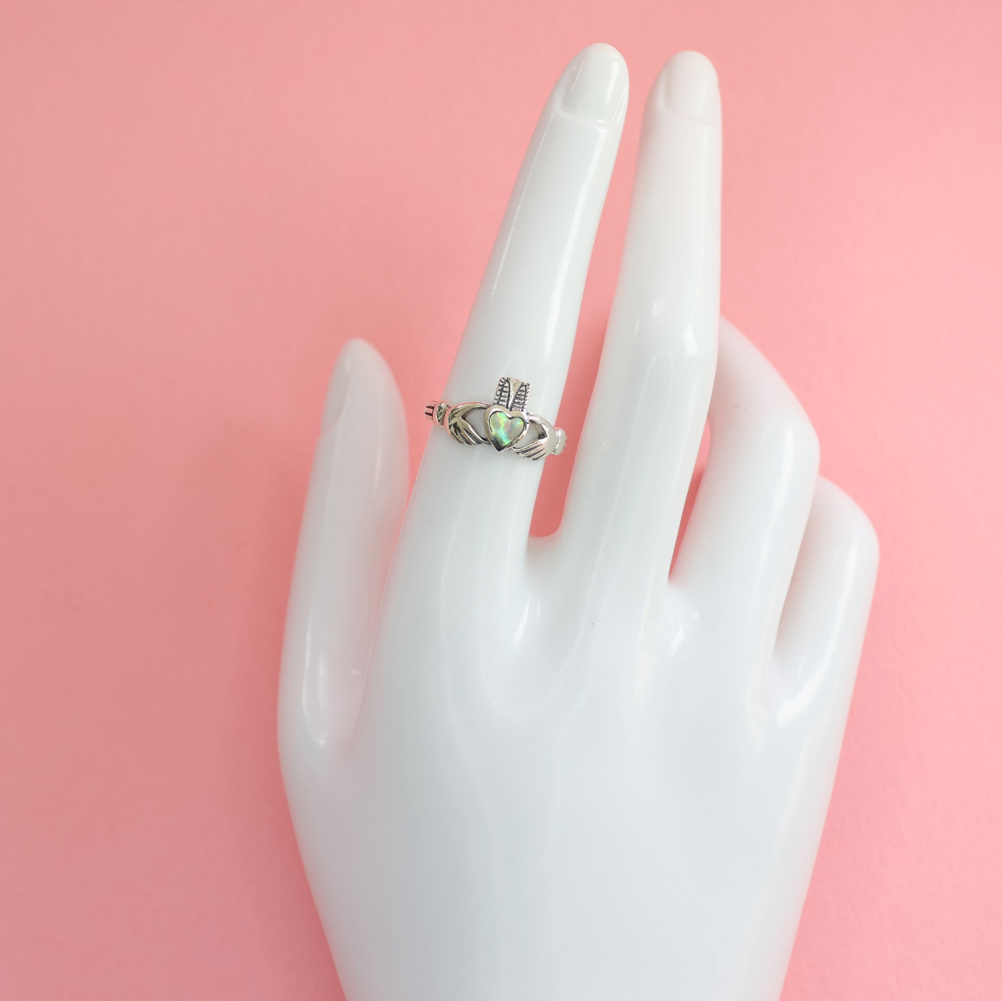 Stylish Silver Claddagh Ring displayed on a hand mannequin against a pink background