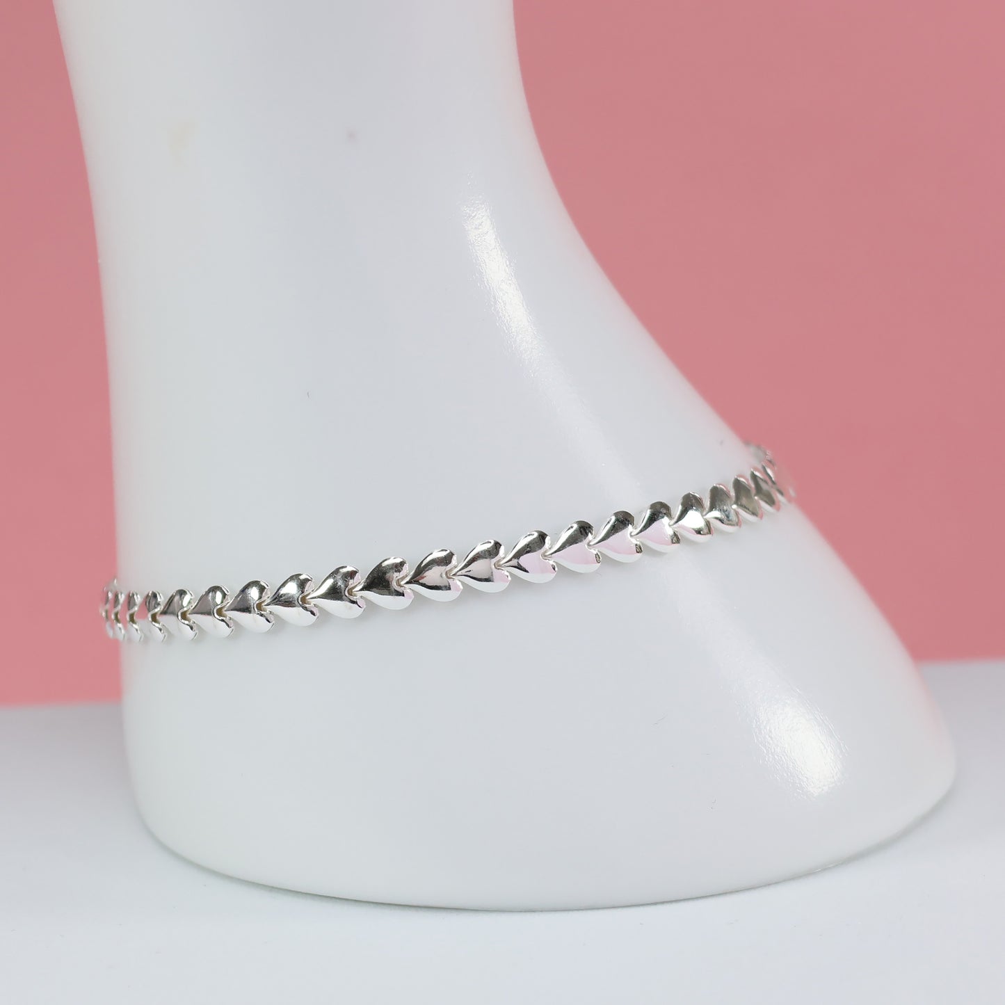 Stylish silver heart link bracelet displayed on a white stand against a pink background