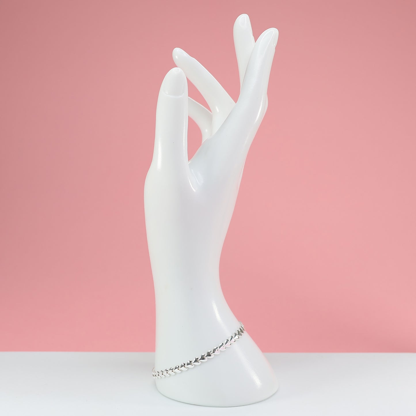 Elegant silver heart link bracelet displayed on a mannequin hand against a pink background