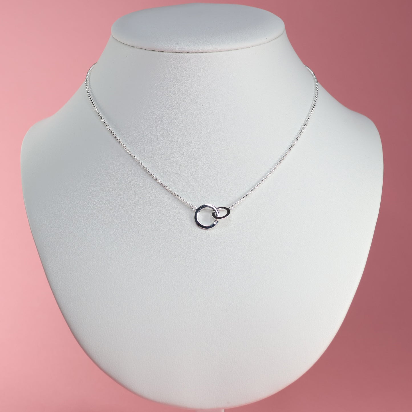 Elegant silver interlocking hoop necklace displayed on a white bust against a pink background