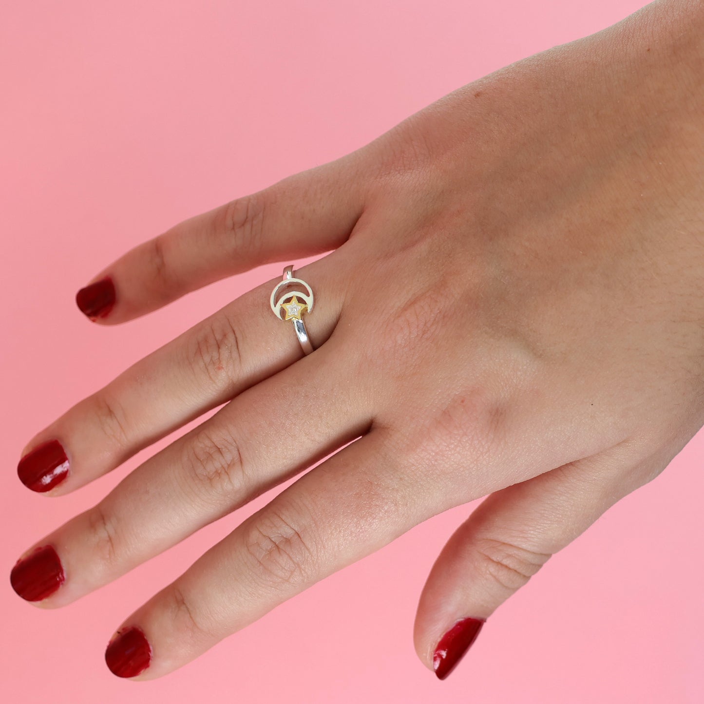 Silver moon and star ring displayed on a hand with polished nails against a pink background