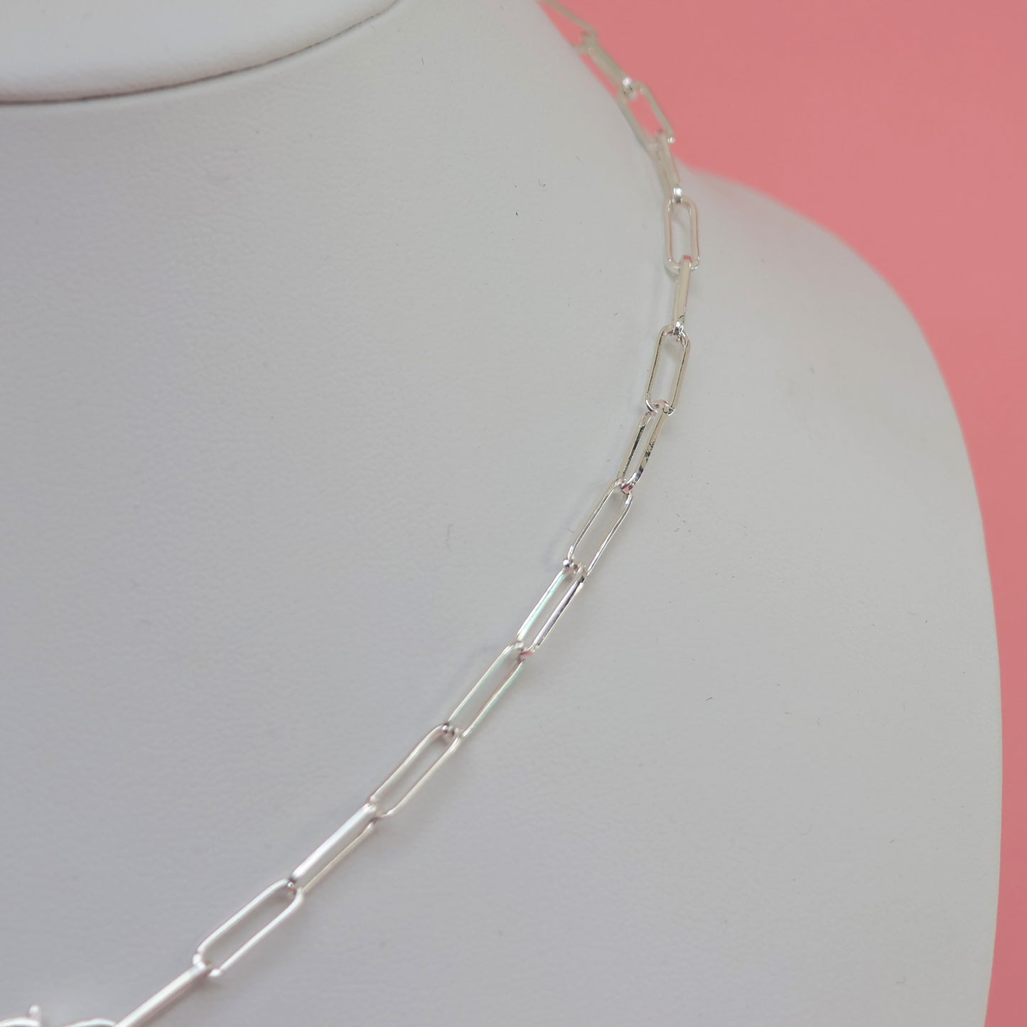 Elegant silver necklace with heart clasp displayed on a bust against a pink background
