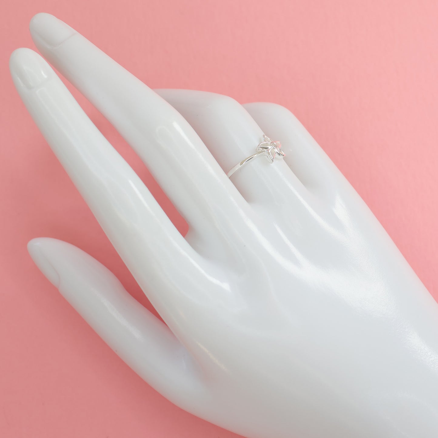Elegant silver star flower ring displayed on a hand-shaped mannequin against a pink background