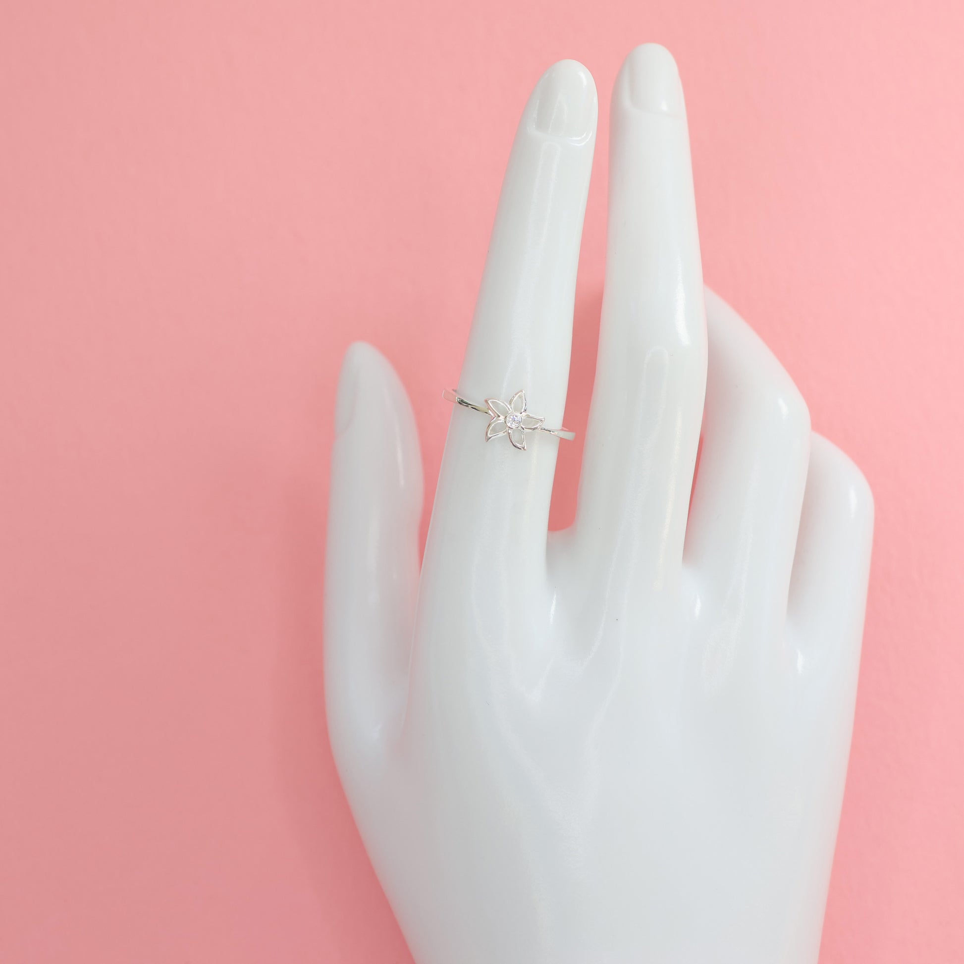 Elegant silver star flower ring displayed on a hand model against a pink background