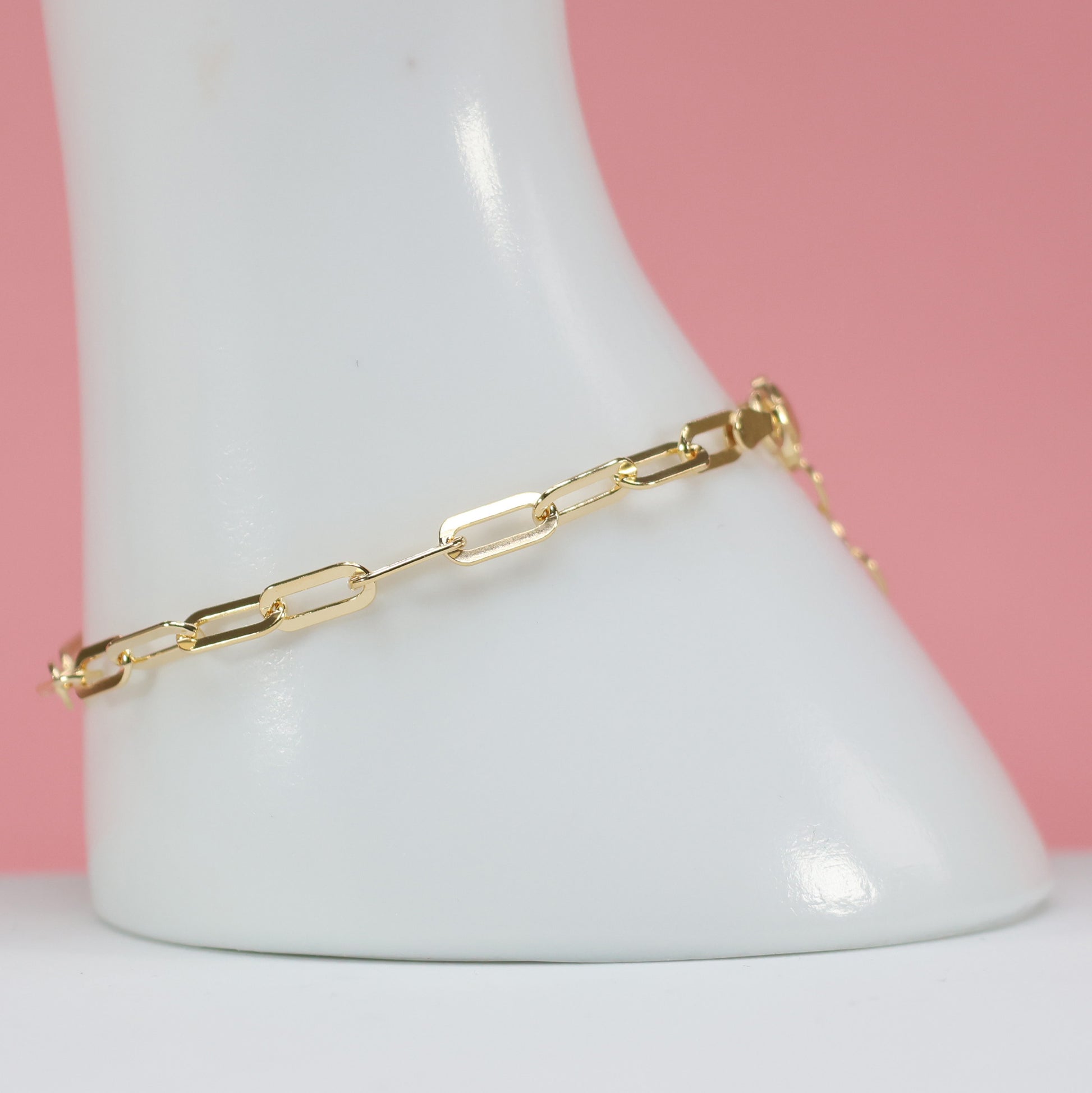 Elegant gold plated paperclip bracelet showcased on a white display with pink background