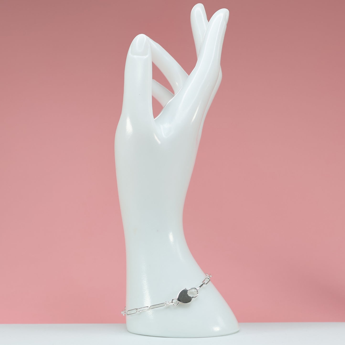 Stylish heart clasp silver bracelet displayed on a white hand mannequin against a pink background