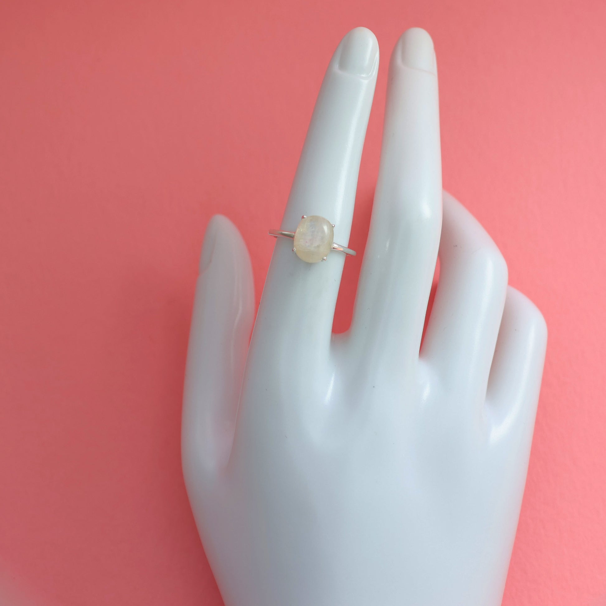 Elegant large moonstone silver ring displayed on a hand model against a pink background