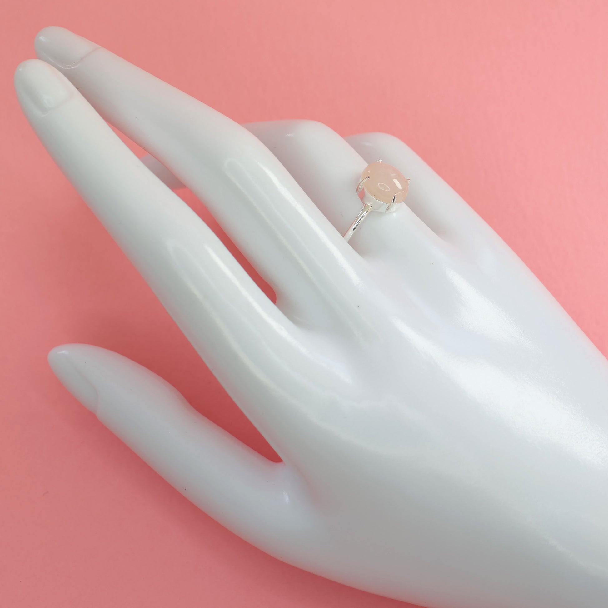 Elegant large rose quartz silver ring displayed on a hand against a pink background