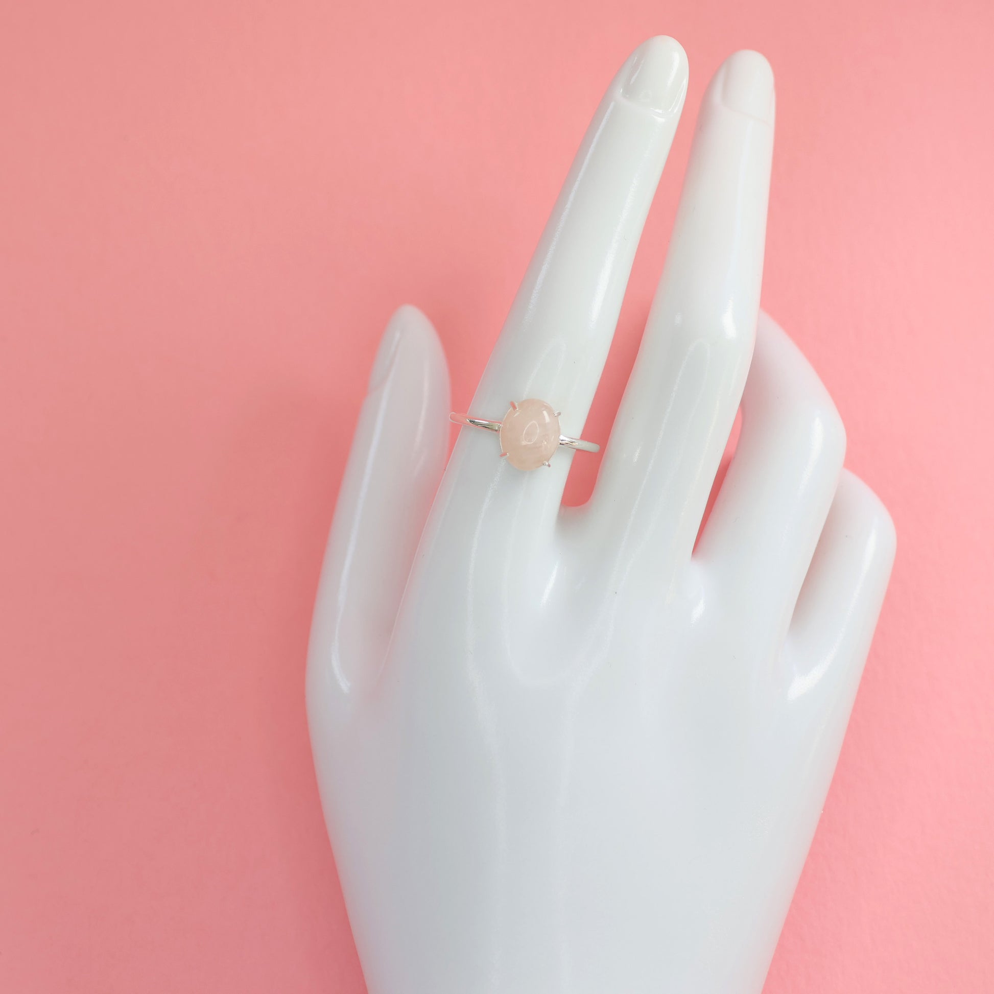 Large rose quartz silver ring displayed on a hand mannequin against a pink background