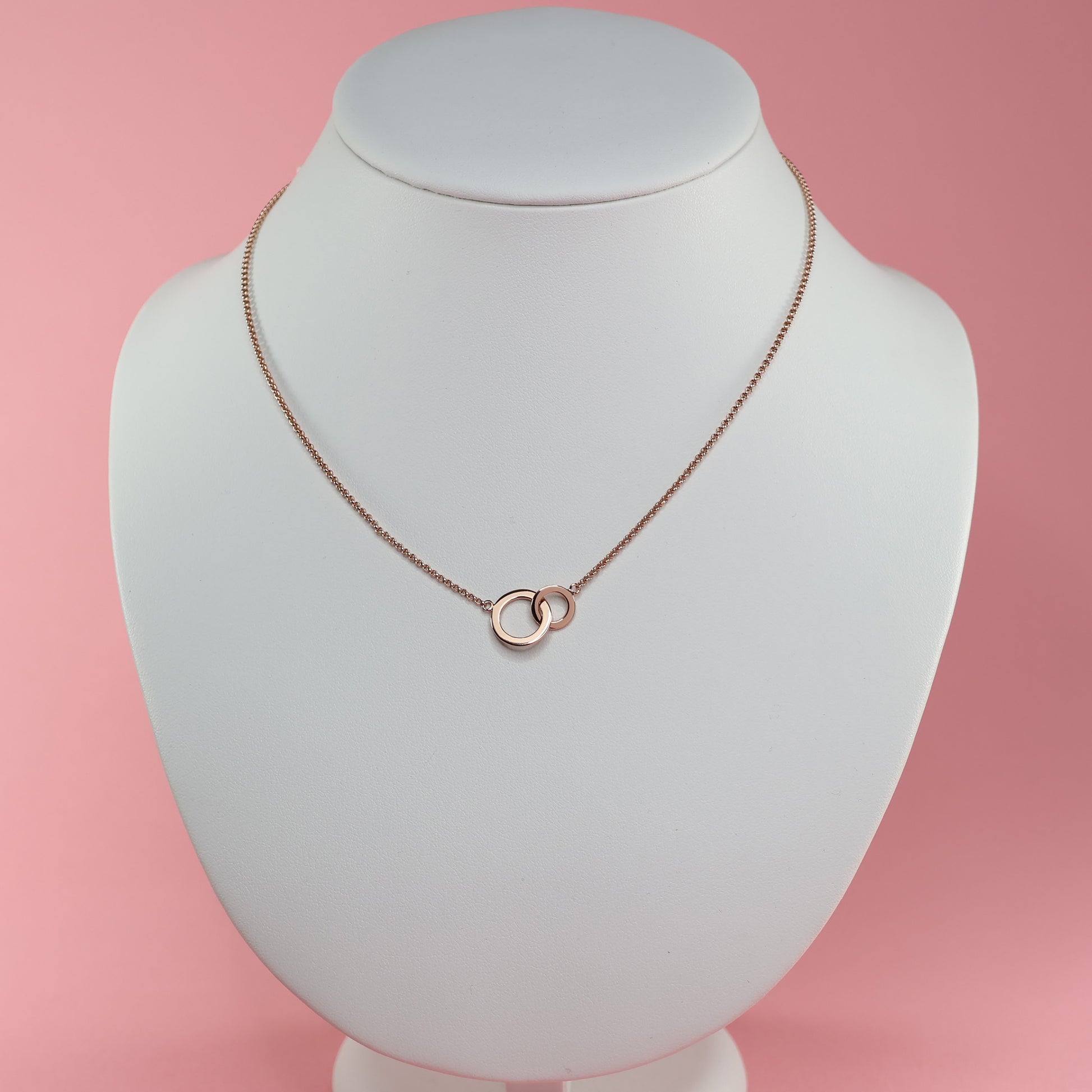 Elegant rose gold double hoop pendant necklace on a display bust against a pink background