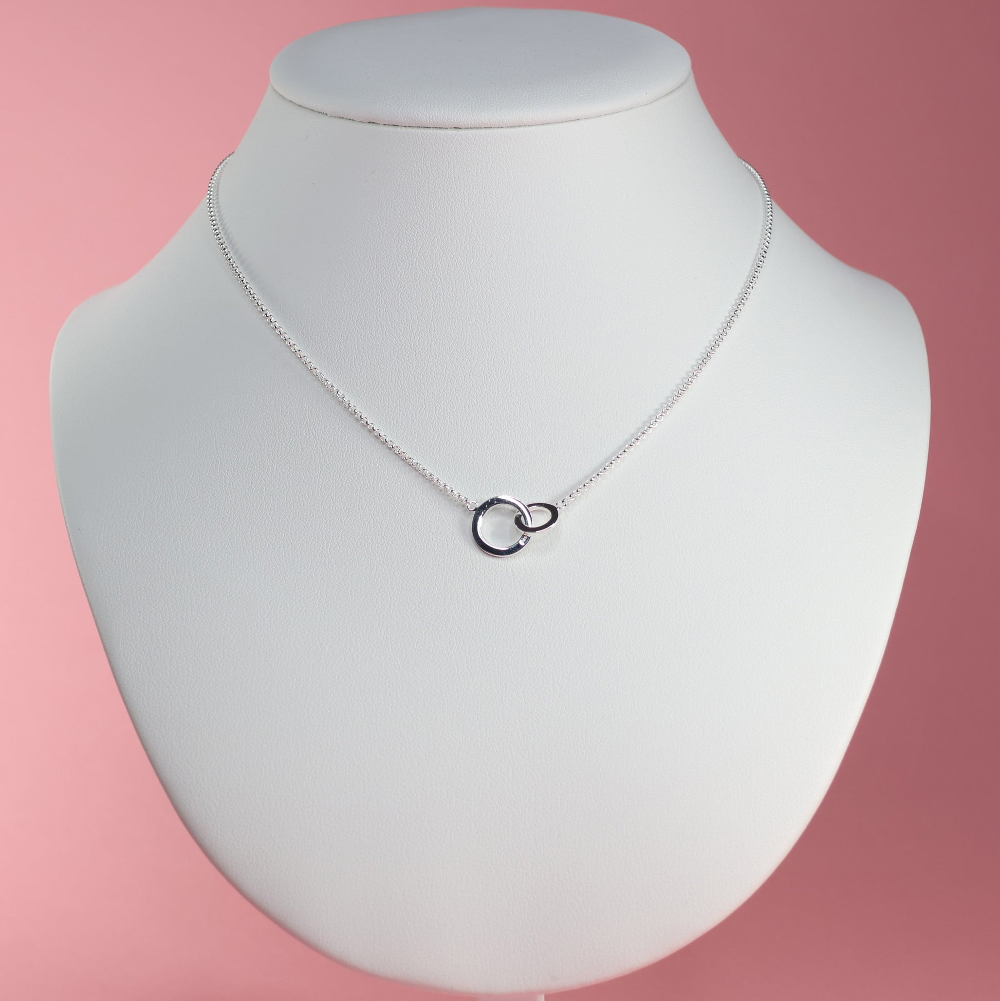 Elegant silver interlocking hoop necklace displayed on a white bust against a pink background