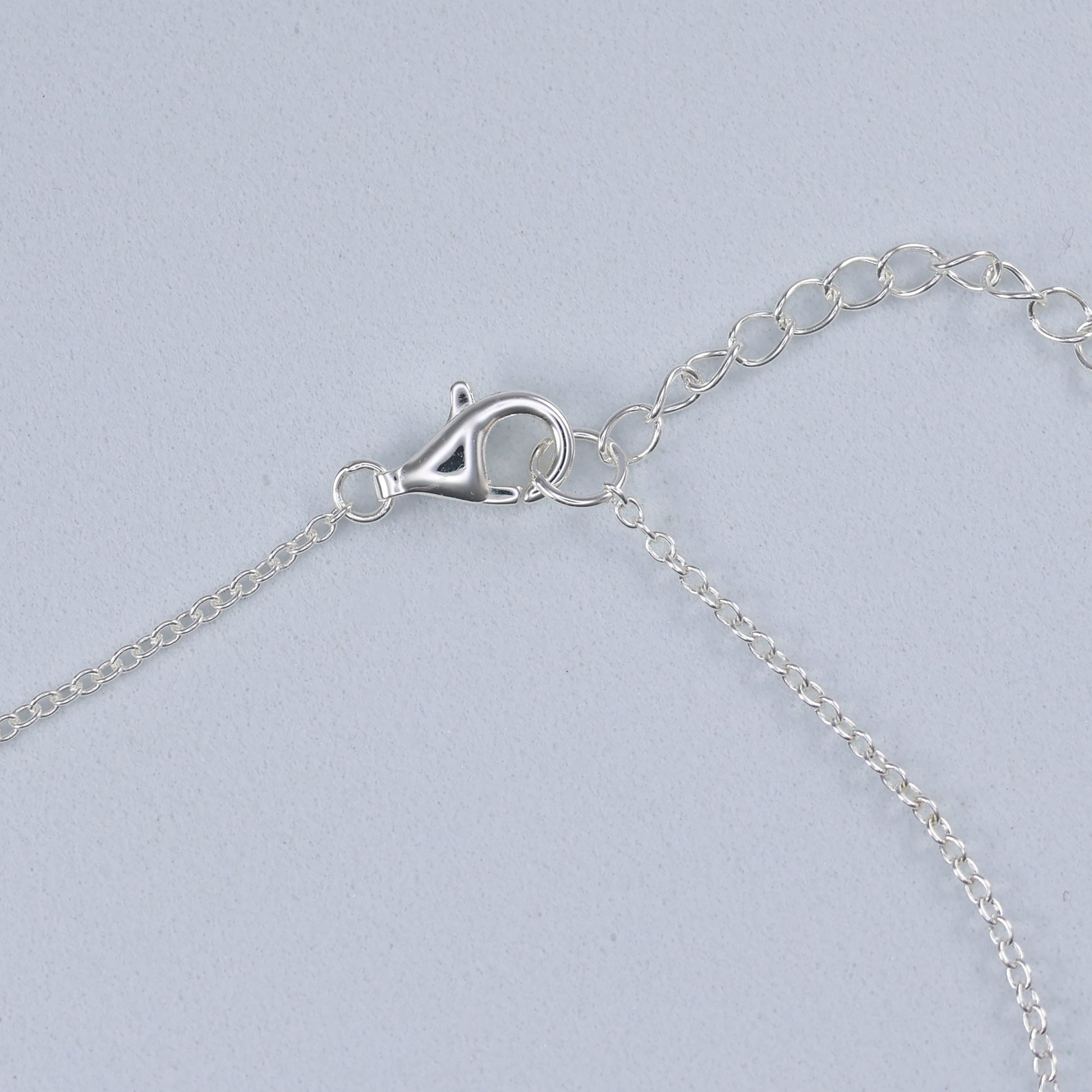 Close-up of clasp on a silver necklace with blue clover, showcasing intricate chain design