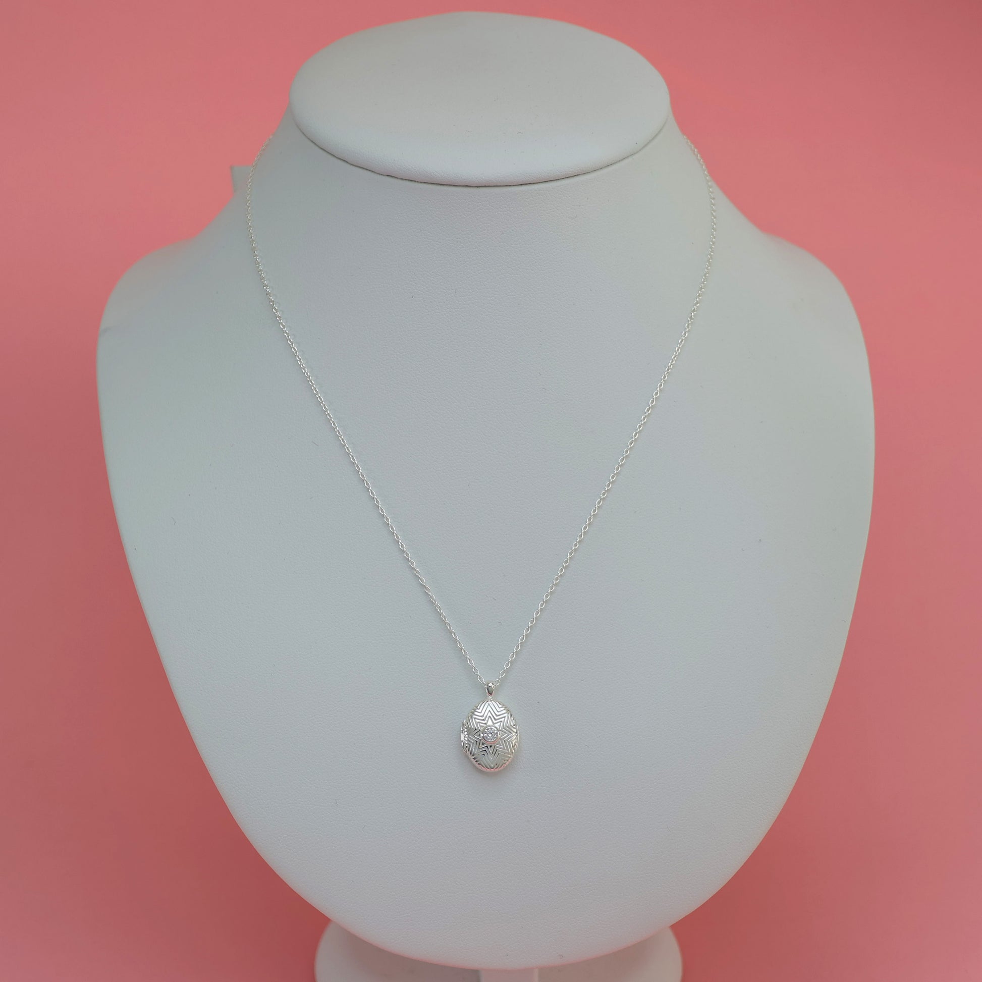Elegant silver oval locket necklace displayed on a white bust against a pink background